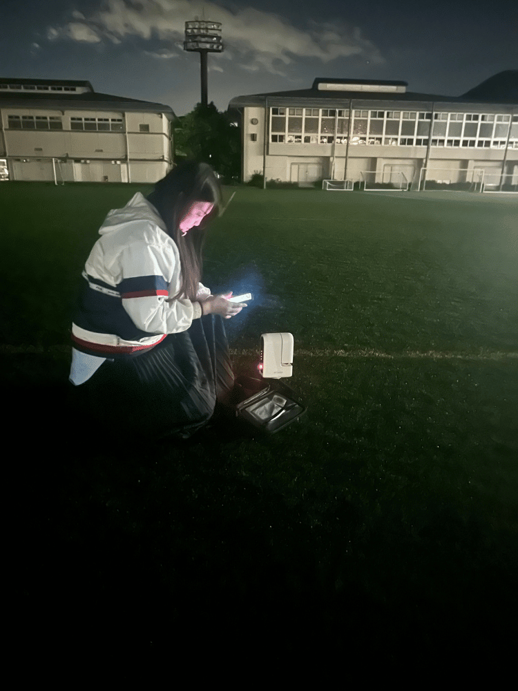 夜のグラウンドに置かれた天体望遠鏡コントローラーとモバイルバッテリー